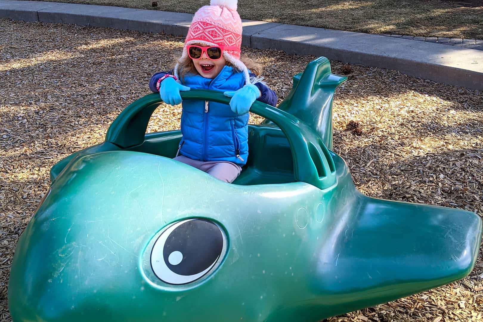 A toddler enjoys playing on a toy airplane at a playground.
