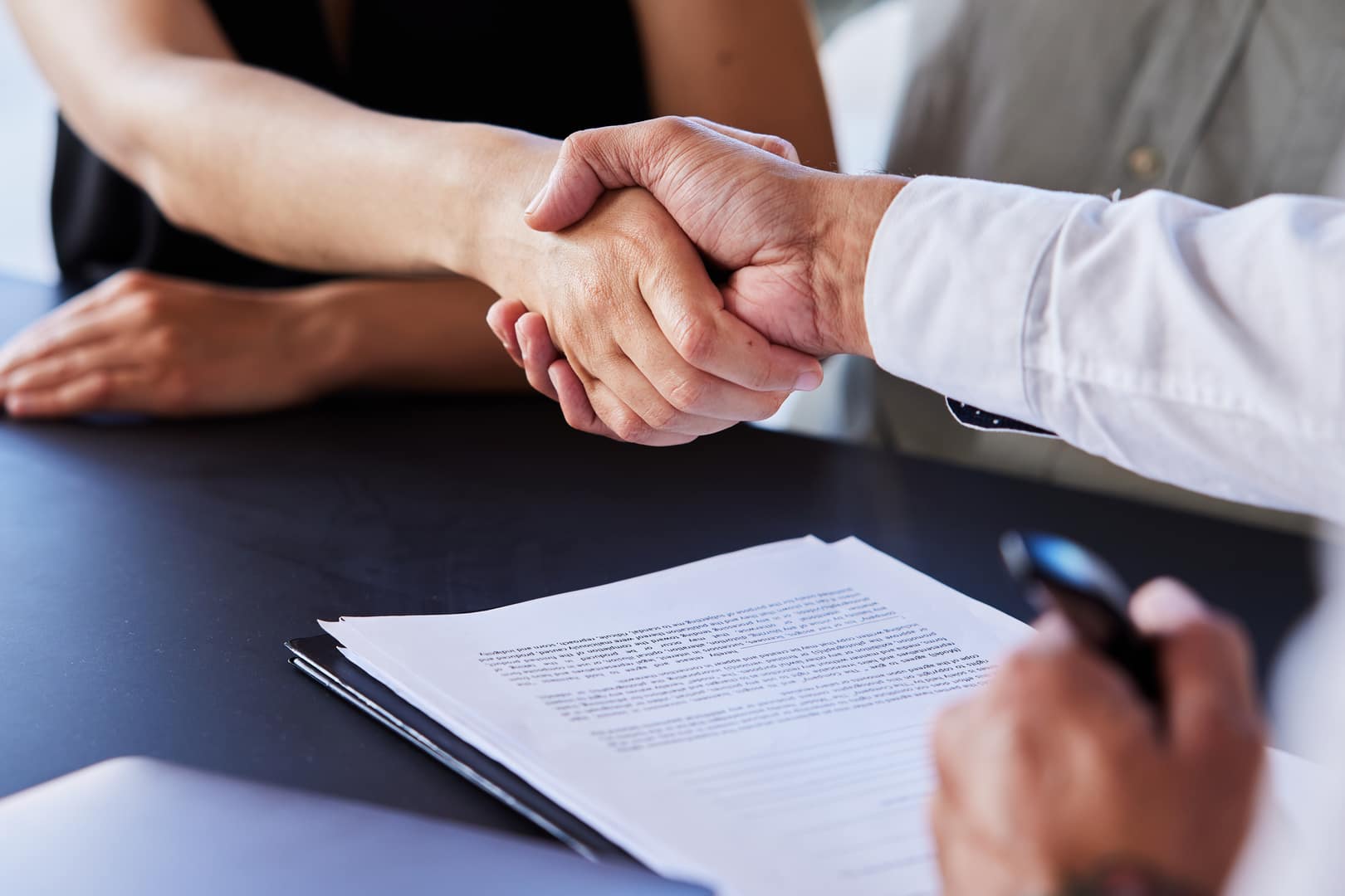 Two people shake hands over a stack of estate planning documents.